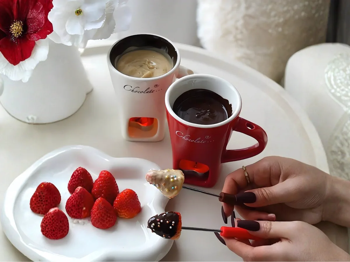 White chocolate in one mug and dark chocolate in another, two forks lifting dipped strawberries covered in sprinkles.
